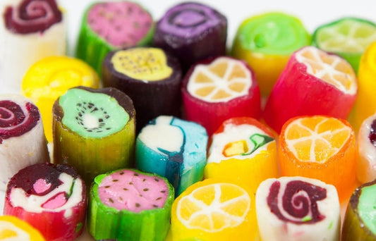 “Close-up of colourful assorted rock candies with detailed fruit designs such as lemon, kiwi, strawberry, and blueberry, arranged in a bright, glossy pile.”