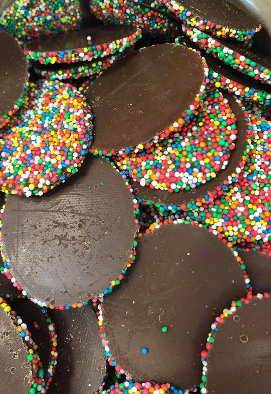Large round milk chocolate discs topped with colourful hundreds and thousands, displayed on a white background.