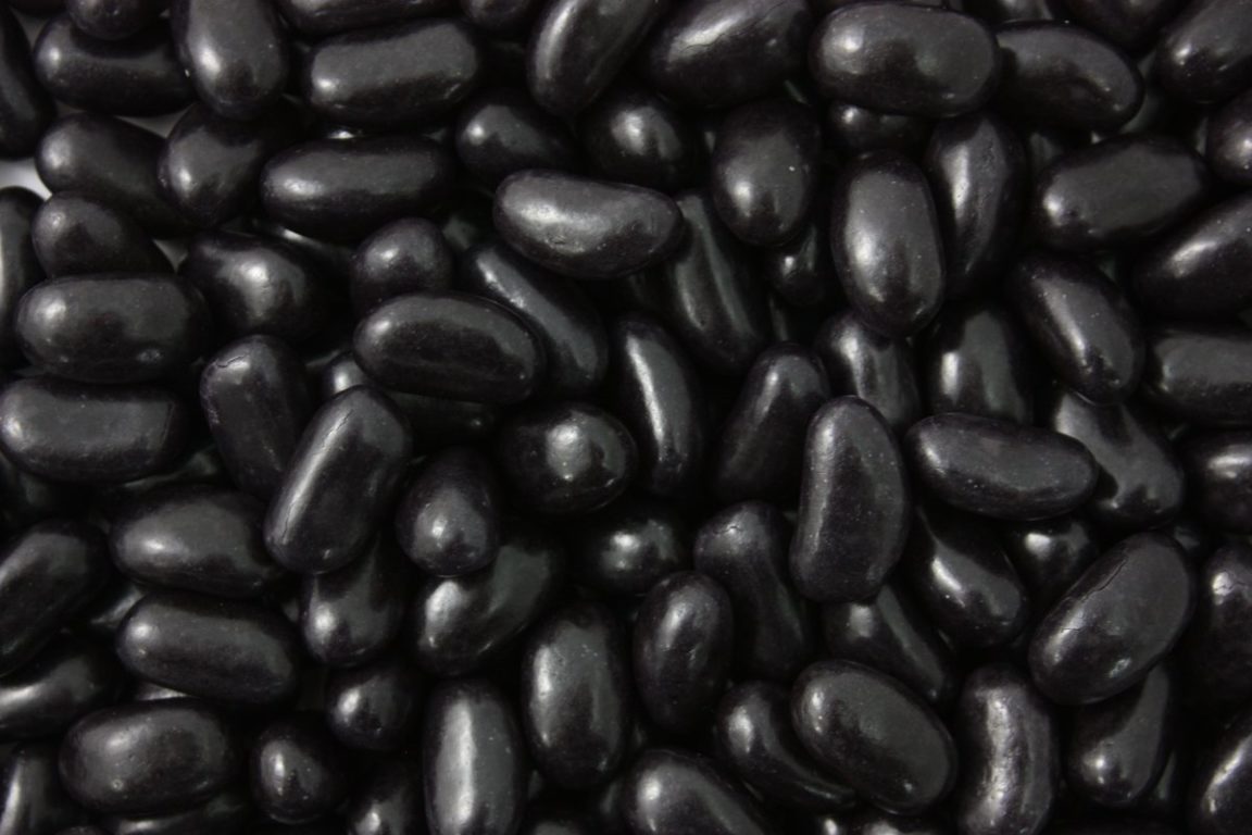 “Close-up image of glossy black jelly beans with a smooth coating and chewy texture, displayed on a white background.”