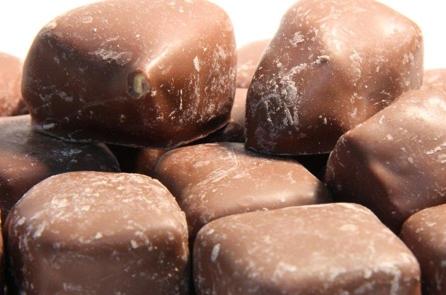 Bite-sized chunks of golden honeycomb coated in smooth milk chocolate, displayed on a white background.