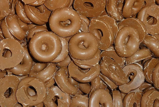 Chocolate-coated aniseed rings stacked together on a white background, showing glossy brown coating and circular shape.