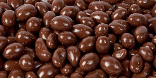 Milk chocolate-coated peanuts piled together on a white background, showing glossy brown coating and smooth round shapes.