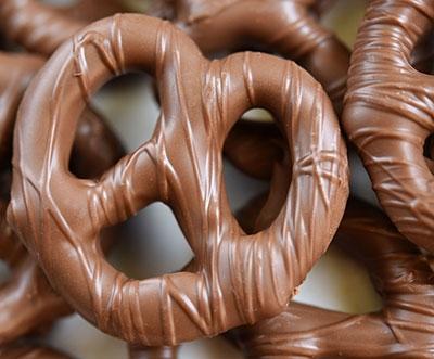 Milk chocolate-coated pretzels piled together, showing a glossy brown coating and crunchy twisted shape on a white background.