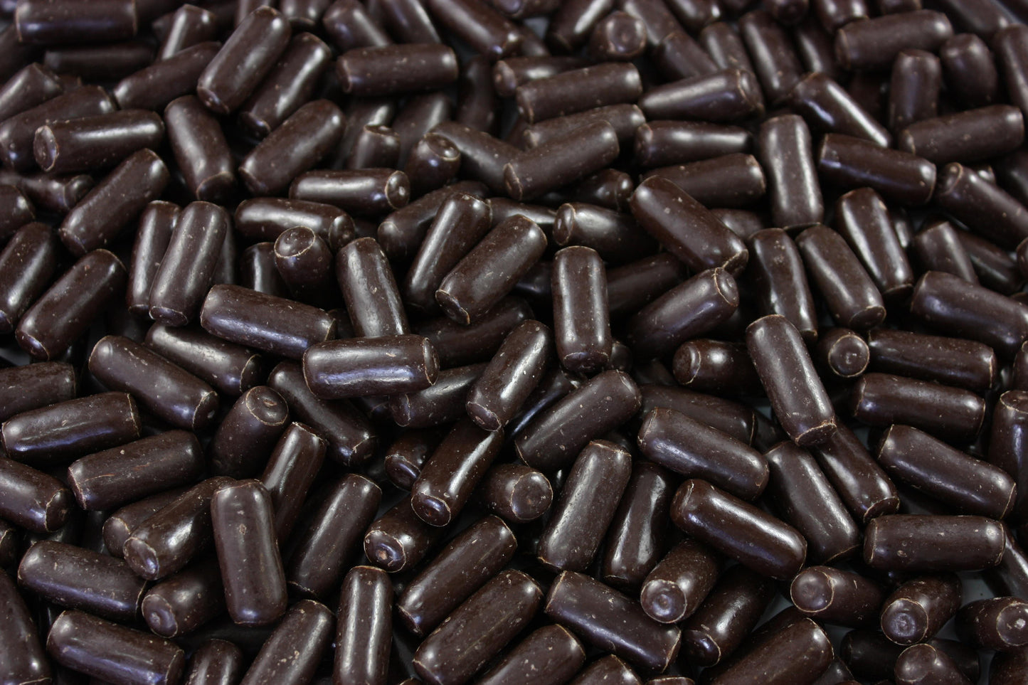 “Close-up of dark chocolate-coated licorice bullets with a glossy finish, displayed on a white background for a professional confectionery product image.”