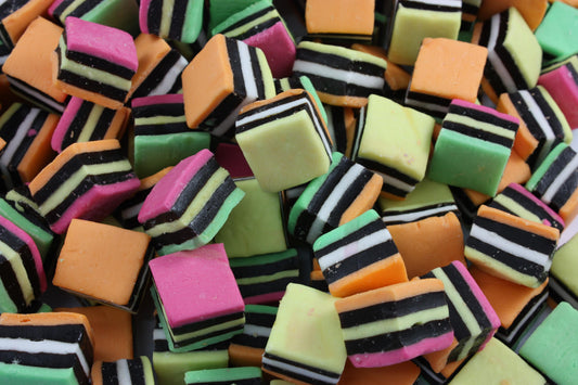 “Assorted licorice allsorts in bright colours — layered and striped pieces of soft licorice candy mixed with coconut, fondant, and jelly textures on a white background.”