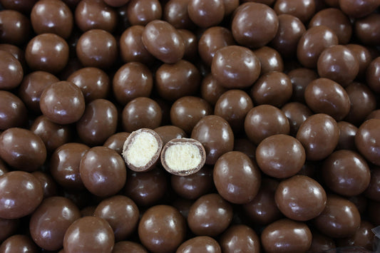 “Close-up of glossy chocolate-coated malt balls in rich brown tones, piled together on a clean white background.”