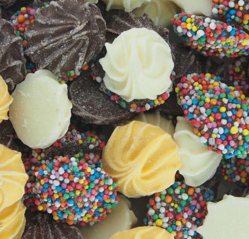 Assorted milk and white chocolate whirls topped with colourful hundreds and thousands, displayed together on a white background.