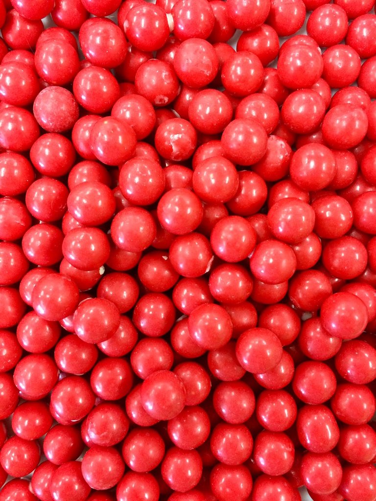 “Close-up of shiny orange chocolate drops with a smooth candy shell and glossy finish, piled together on a white background.”