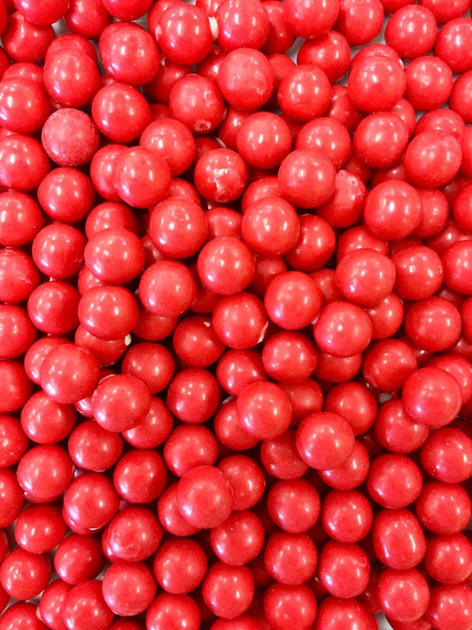 “Close-up of shiny orange chocolate drops with a smooth candy shell and glossy finish, piled together on a white background.”