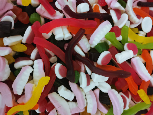 Colourful assortment of mixed lollies including snakes, milk bottles, raspberries, teeth, and jelly shapes displayed on a white background.