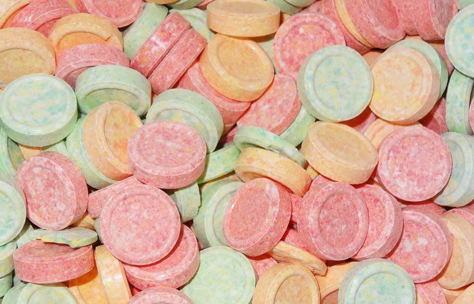 Assorted round UFO-shaped hard fizzy candies in pastel colours including pink, orange, yellow, and green, arranged closely together on a white background.