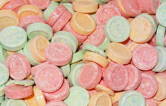 Assorted round UFO-shaped hard fizzy candies in pastel colours including pink, orange, yellow, and green, arranged closely together on a white background.