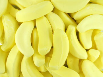 Soft, bright yellow banana-shaped lollies displayed on a white background, showing smooth, foamy texture.