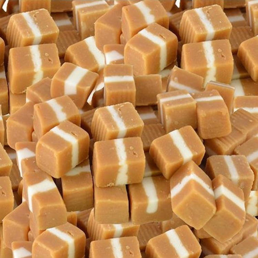 Soft, square caramel lollies with creamy white layers stacked together on a white background, showing smooth and chewy texture.