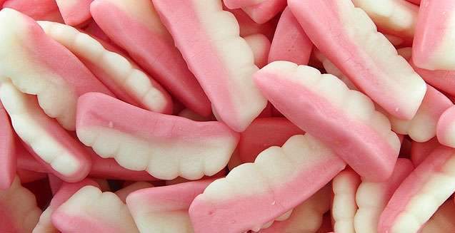 Pink and white gummy teeth-shaped lollies displayed on a white background, showing their soft and chewy foam texture.