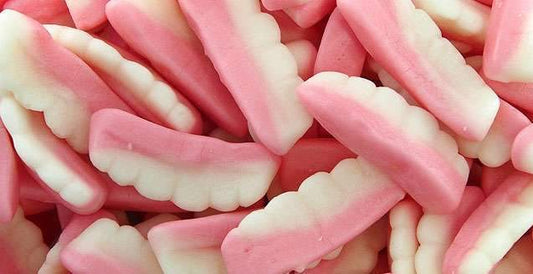 Pink and white gummy teeth-shaped lollies displayed on a white background, showing their soft and chewy foam texture.
