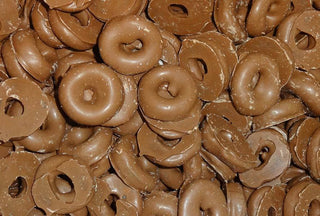 Chocolate-coated aniseed rings stacked together on a white background, showing glossy brown coating and circular shape.