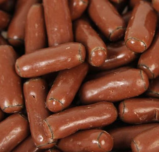 Chocolate-coated licorice bullets arranged closely together on a white background, showing glossy milk chocolate coating.