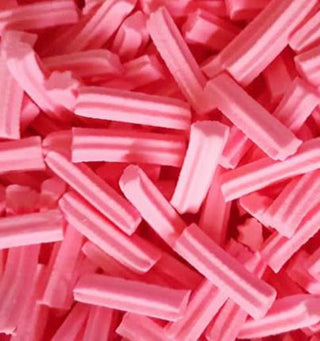 Pink mini musk stick lollies piled together on a white background, showing their smooth, pastel pink texture and cylindrical shape.
