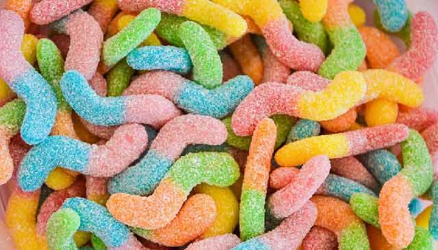 Colourful sour gummy worms coated in sugar, displayed on a white background, showing their bright rainbow colours and tangy texture.