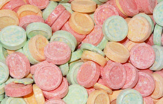 Assorted round UFO-shaped hard fizzy candies in pastel colours including pink, orange, yellow, and green, arranged closely together on a white background.