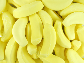 Soft, bright yellow banana-shaped lollies displayed on a white background, showing smooth, foamy texture.