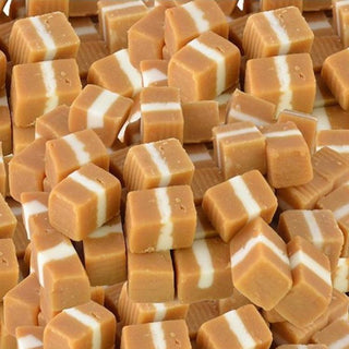 Soft, square caramel lollies with creamy white layers stacked together on a white background, showing smooth and chewy texture.